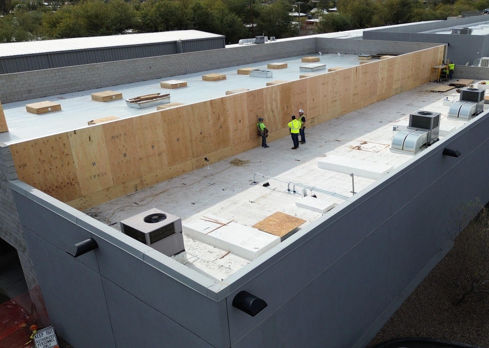 Aerial view of a dealership roof during construction, with workers and parked cars alongside