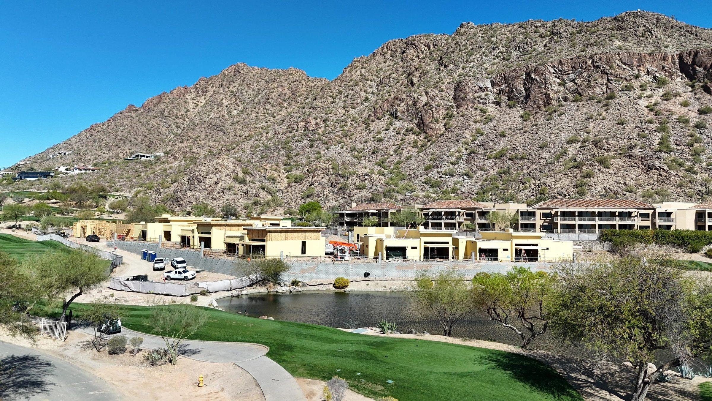 Resort villas under construction at the foot of a desert mountain, beside a golf course pond