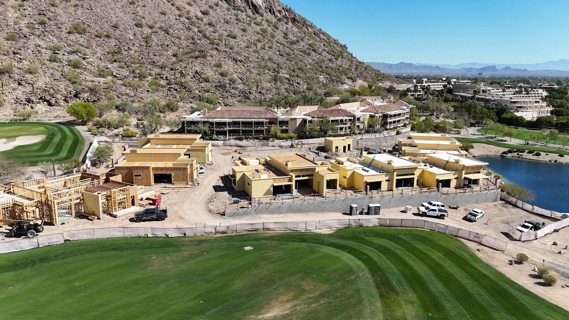 Aerial view of resort villas under construction beside a golf fairway, with a mountain behind