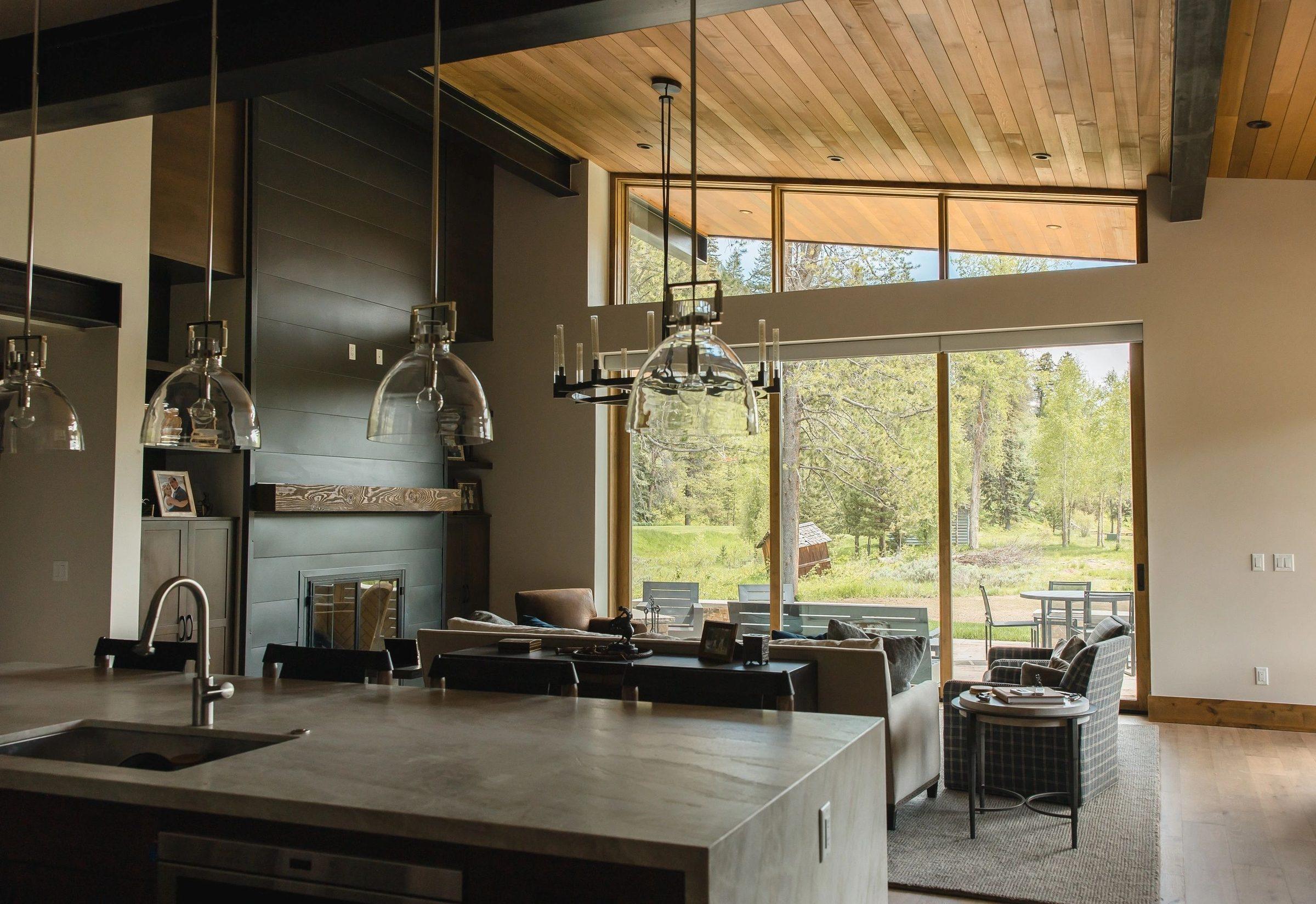 A finished kitchen and great room with a timber ceiling and tall windows onto pine trees