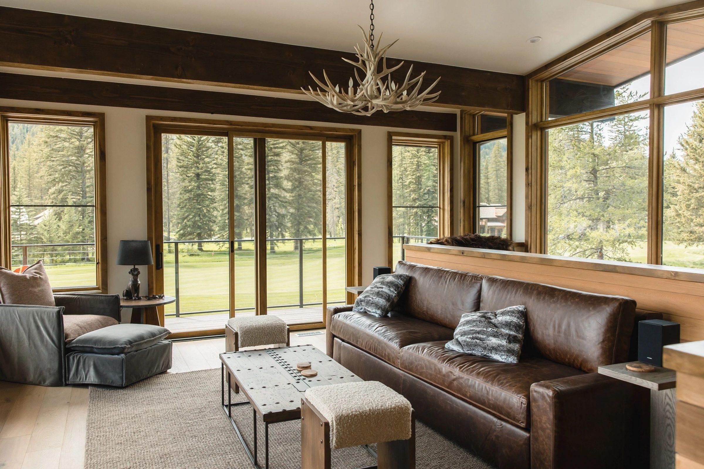 A finished lounge with leather sofas, an antler chandelier and windows onto a golf course