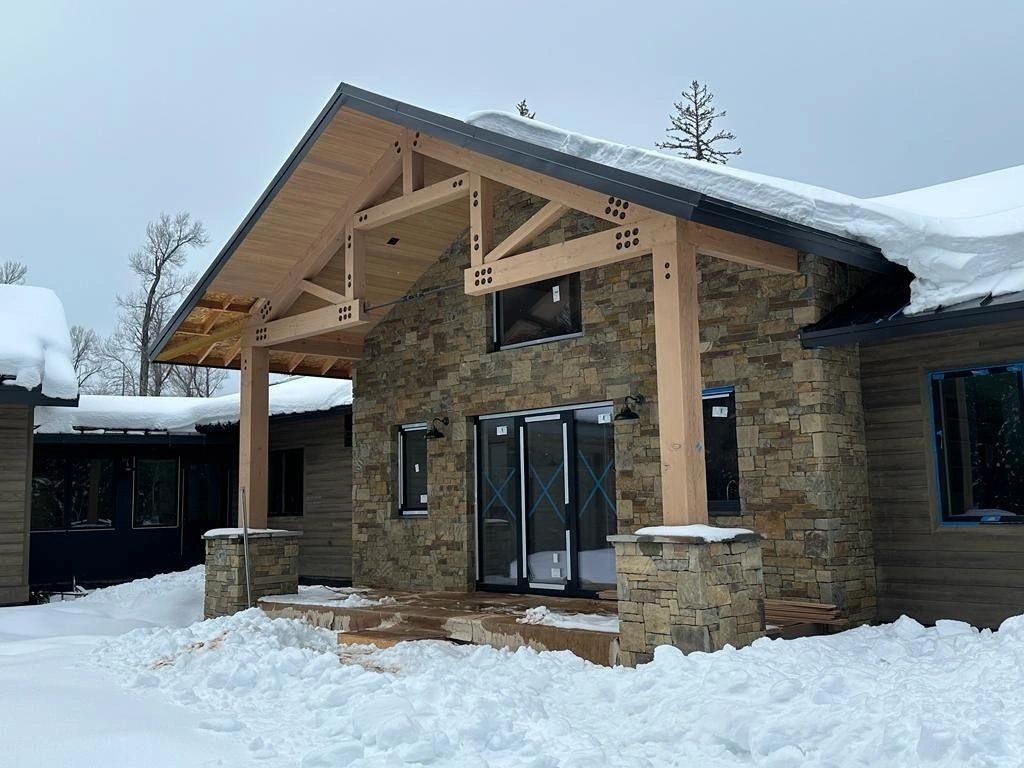 The timber-framed stone entry of a mountain home in snow, nearing completion